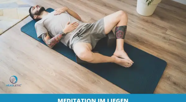Mann mit Tattoos entspannt sich im Liegen auf einer Yogamatte, umgeben von Holzboden und einer Pflanze. Perfekt für Meditation im Liegen.