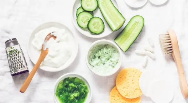 Zutaten für eine Gurkenmaske selber machen: Gurkenscheiben, Joghurt, geriebene Gurke, ein Hobel und weitere Utensilien.