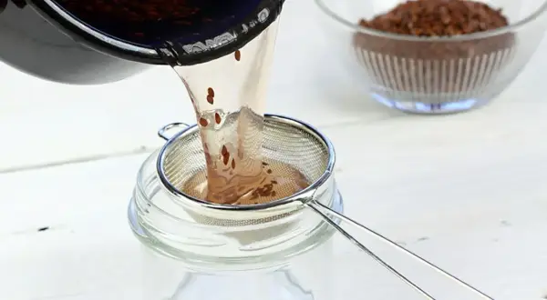 Flüssigkeit mit Leinsamen wird durch ein Sieb in ein Glas gegossen. Perfekt für leinsamen gesichtscreme selber machen.