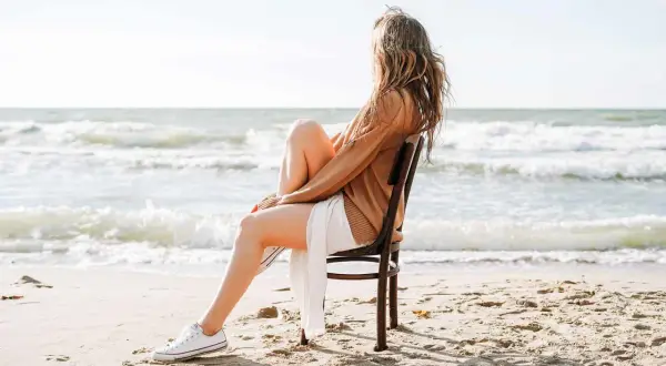 Frau sitzt am Strand auf einem Stuhl und blickt aufs Meer. Sie fragt sich, wie werde ich geduldiger, während sie die Wellen beobachtet.