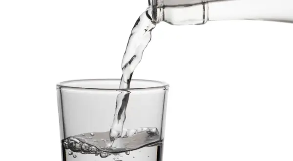 Klares Wasser fließt aus einer Flasche in ein Glas. Die erfrischende birkenwasser wirkung wird durch die sprudelnden Bläschen im Glas angedeutet.