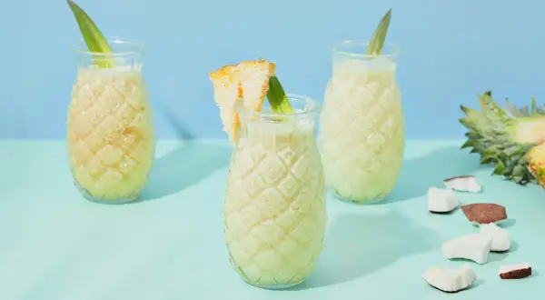 Erfrischende Kokoswasser Rezepte: cremige Drinks in Ananas-Gläsern, garniert mit Ananasblatt und Kokosstückchen.