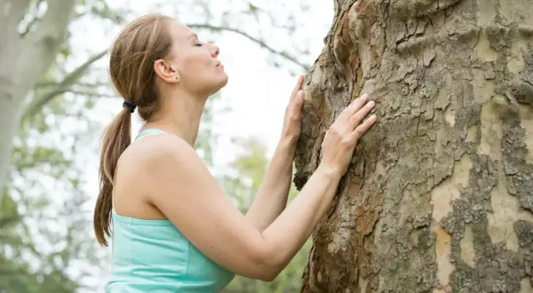 Frau umarmt einen Baum, um achtsam zu sein und die Natur zu spüren.