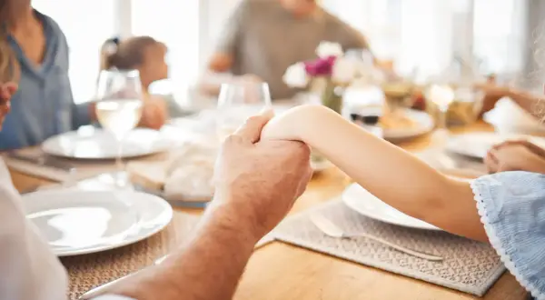 Familie hält Hände vor dem gemeinsamen Abendessen. Ein Moment des Gebets vor dem Essen.