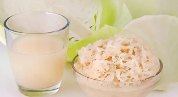 Ein Glas Sauerkrautsaft und eine Schüssel Sauerkraut, um die positive Sauerkrautsaft Wirkung Leber zu unterstützen.