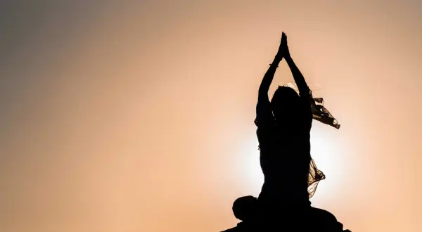 Silhouette einer Person in meditativer Haltung mit erhobenen Händen, die innere Freiheit verkörpert.