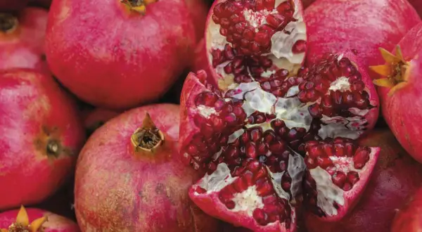Ein aufgeschnittener Granatapfel mit vielen roten Kernen, umgeben von ganzen Früchten. Manche Menschen reagieren empfindlich auf Histamin, das auch im Granatapfel vorkommt.