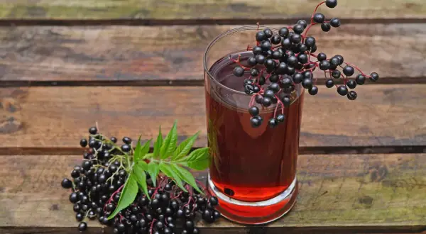 Ein Glas dunkler Holundersaft steht neben frischen Holunderbeeren. Die positive holunder wirkung psyche wird oft durch solche natürlichen Mittel unterstützt.