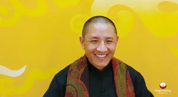 Ein Mann mit Glatze lächelt warm, trägt einen Schal und erklärt die Tummo Meditation.