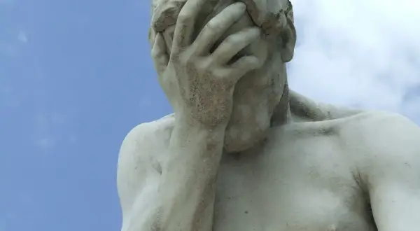 Marmorstatue mit verdecktem Gesicht im blauen Himmel. Ein Symbol für das Aushalten von Schmerzen, Tipps zur Bewältigung.