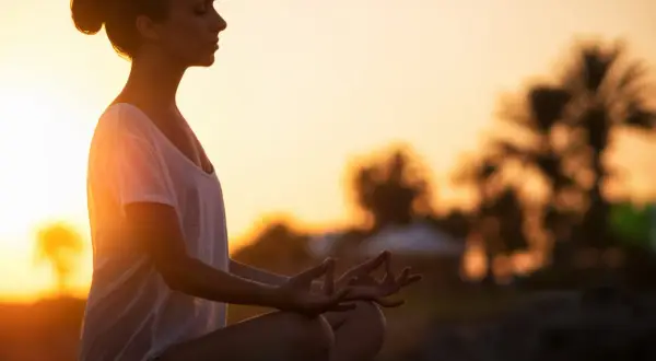 Frau in Meditation am Strand bei Sonnenuntergang, Gedanken loslassen.