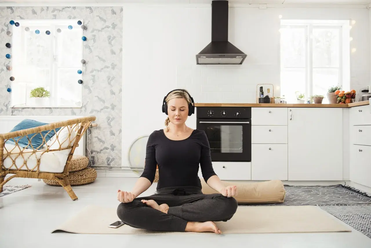 Frau meditiert mit Kopfhörern in einer Küche. Sie folgt einem 3-Minuten-Meditations-Text.