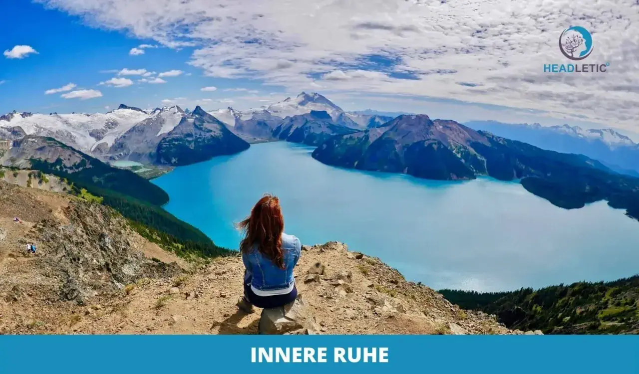Frau meditiert gegen Angst und innere Unruhe auf einem Berg mit Blick auf einen türkisfarbenen See und schneebedeckte Gipfel.