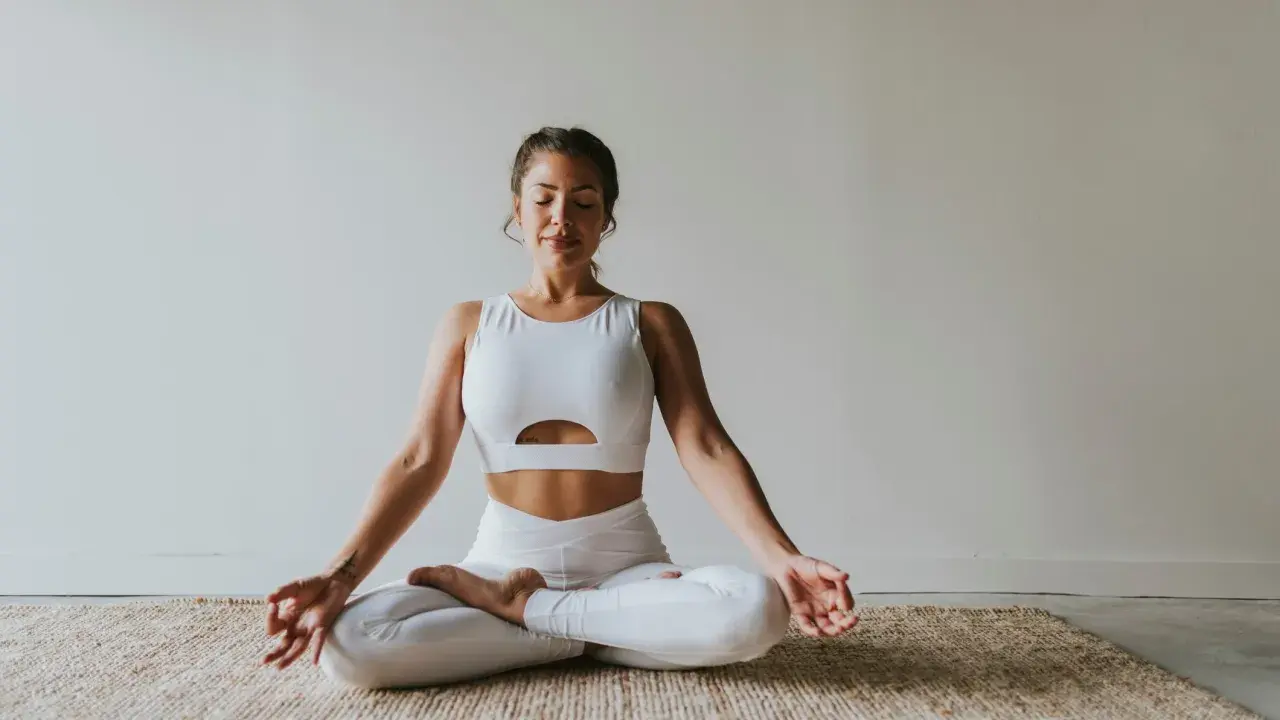 Frau in weißer Sportkleidung praktiziert Meditation. Ihre Augen sind geschlossen, Hände in Mudra-Position. Ein Bild, das Ruhe und Konzentration ausstrahlt, wie in vielen Meditation Studien.