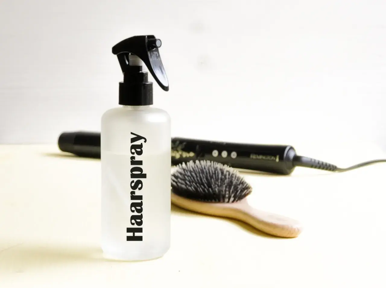Flasche mit "Haarspray" Schriftzug, daneben Haarbürste und Glätteisen. Perfekt für haarspray selber machen.