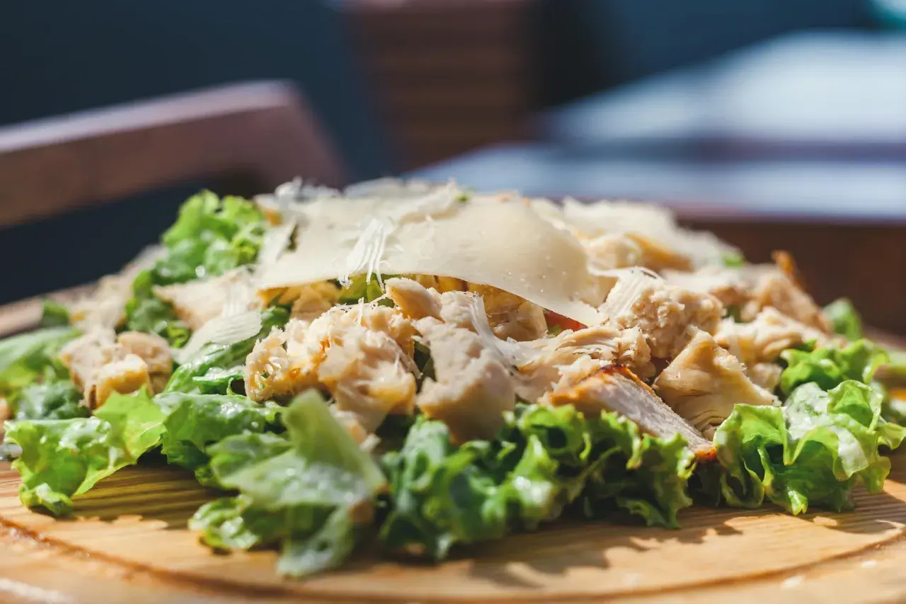 Frischer Romana Salat mit Hähnchenbrust und Parmesan, serviert auf einem Holzbrett.