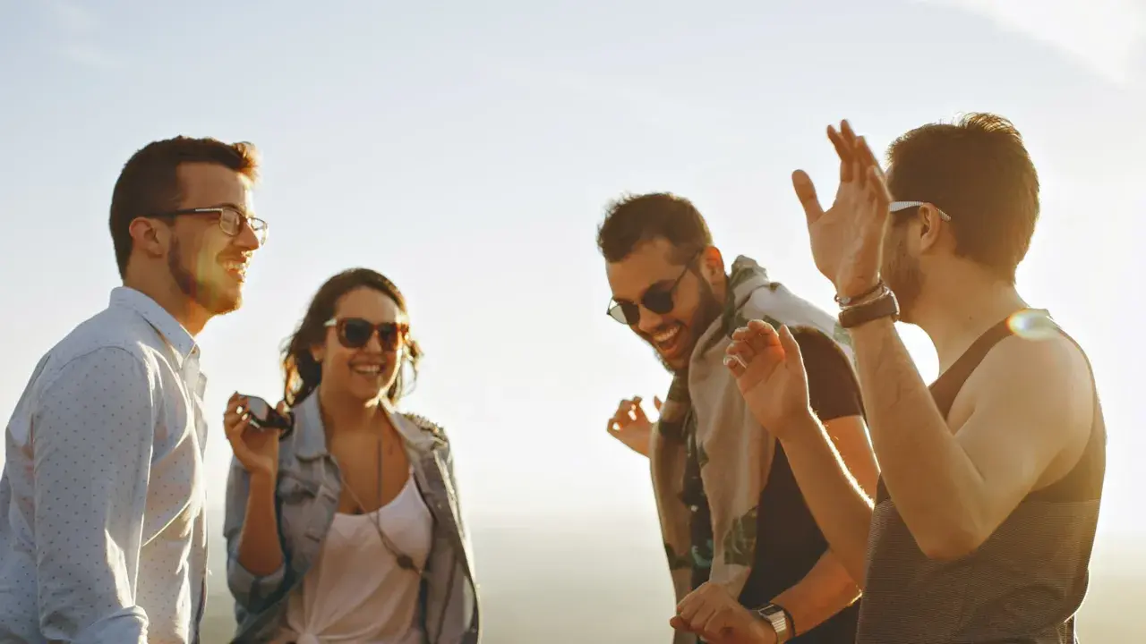 Vier Freunde lachen und tanzen ausgelassen in der Sonne. Sie zeigen, was sind echte freunde: Freude, Gemeinschaft und unbeschwerte Momente.
