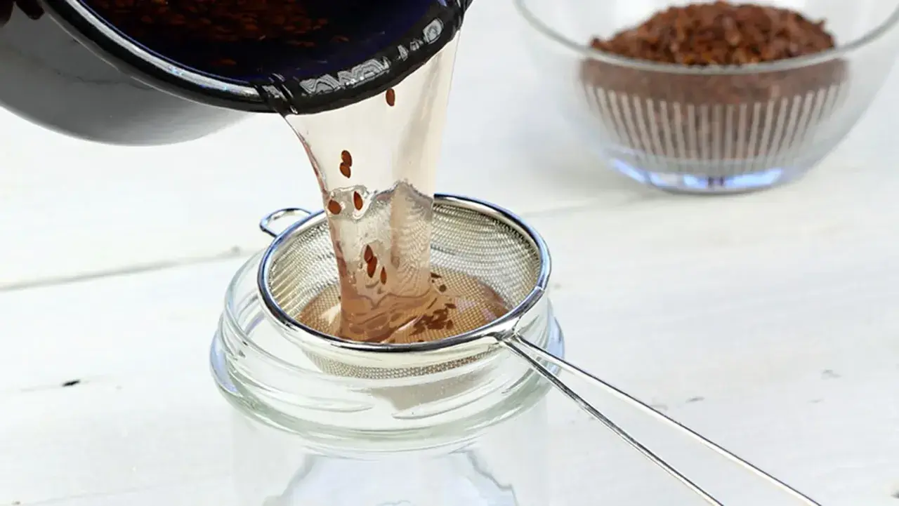 Flüssigkeit mit Leinsamen wird durch ein Sieb in ein Glas gegossen. Perfekt für leinsamen gesichtscreme selber machen.
