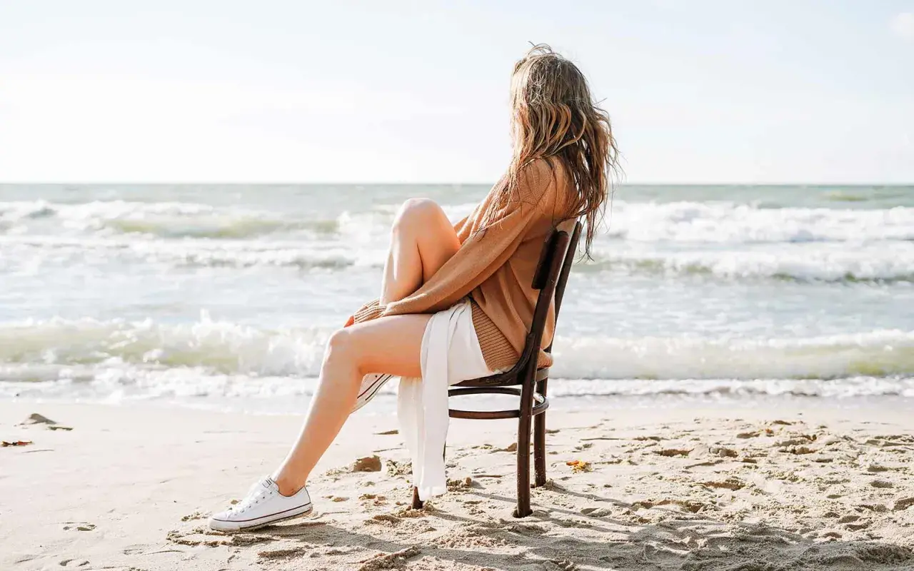 Frau sitzt am Strand auf einem Stuhl und blickt aufs Meer. Sie fragt sich, wie werde ich geduldiger, während sie die Wellen beobachtet.