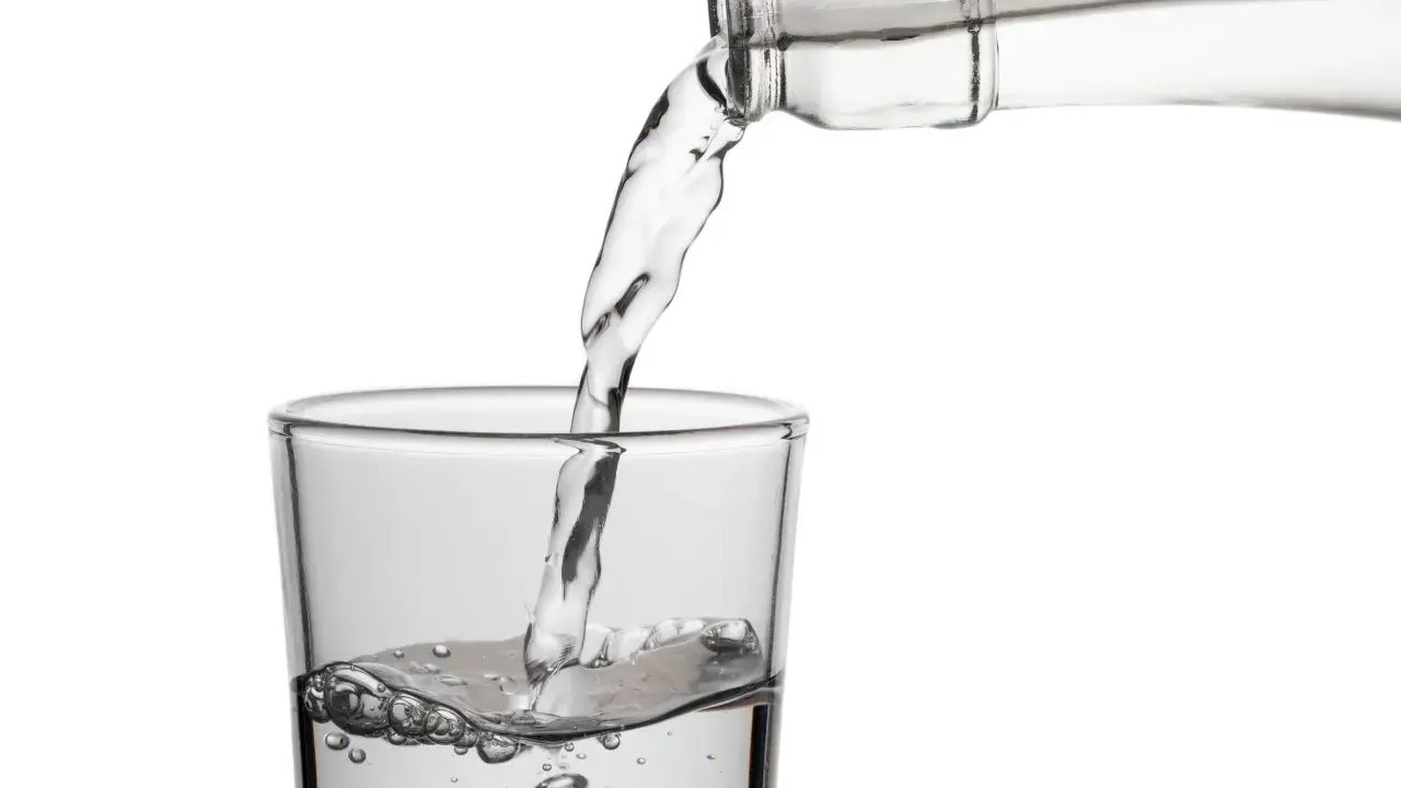 Klares Wasser fließt aus einer Flasche in ein Glas. Die erfrischende birkenwasser wirkung wird durch die sprudelnden Bläschen im Glas angedeutet.