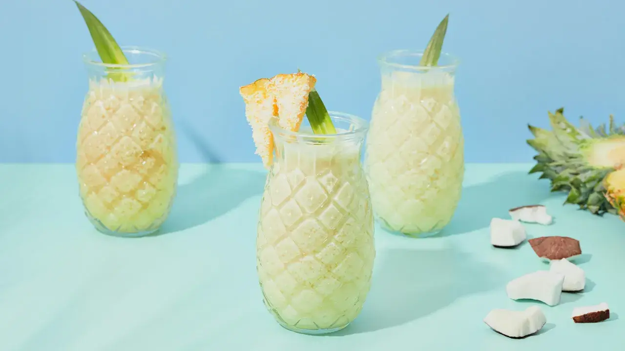 Erfrischende Kokoswasser Rezepte: cremige Drinks in Ananas-Gläsern, garniert mit Ananasblatt und Kokosstückchen.