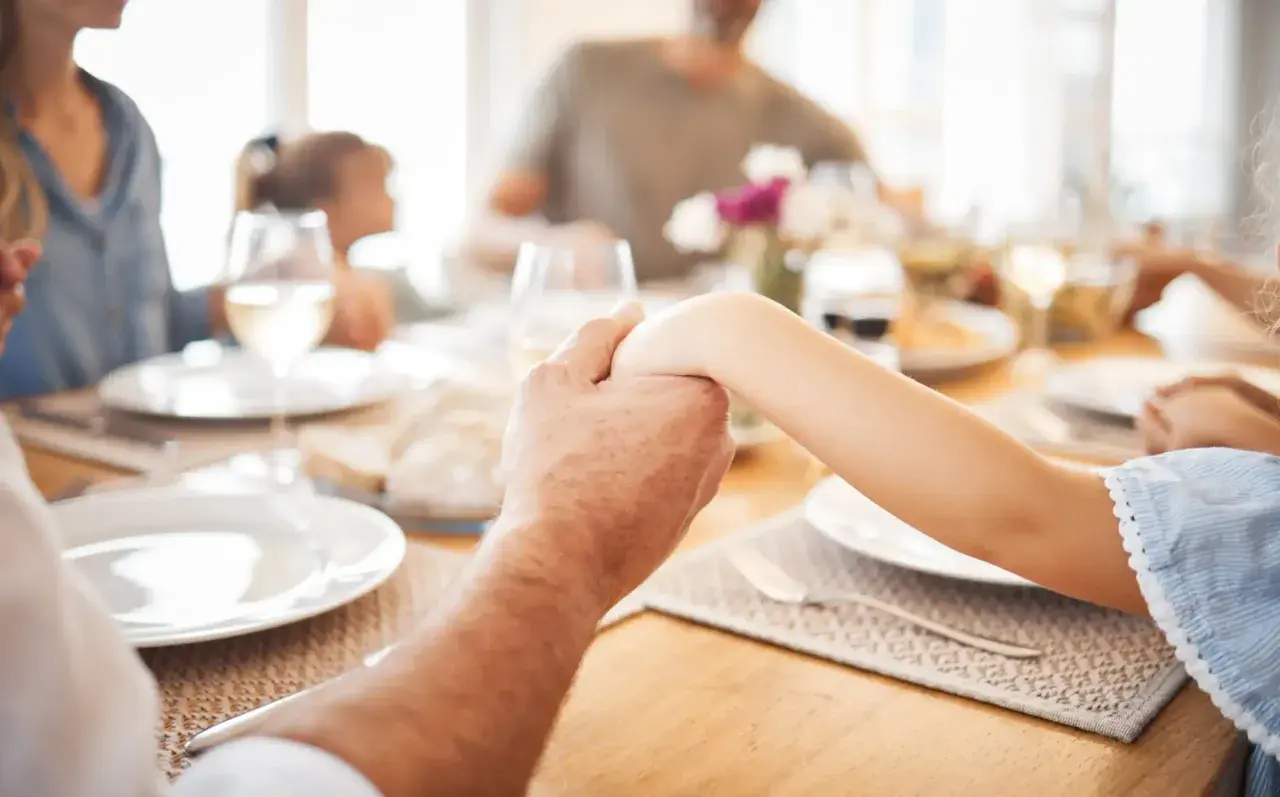 Familie hält Hände vor dem gemeinsamen Abendessen. Ein Moment des Gebets vor dem Essen.