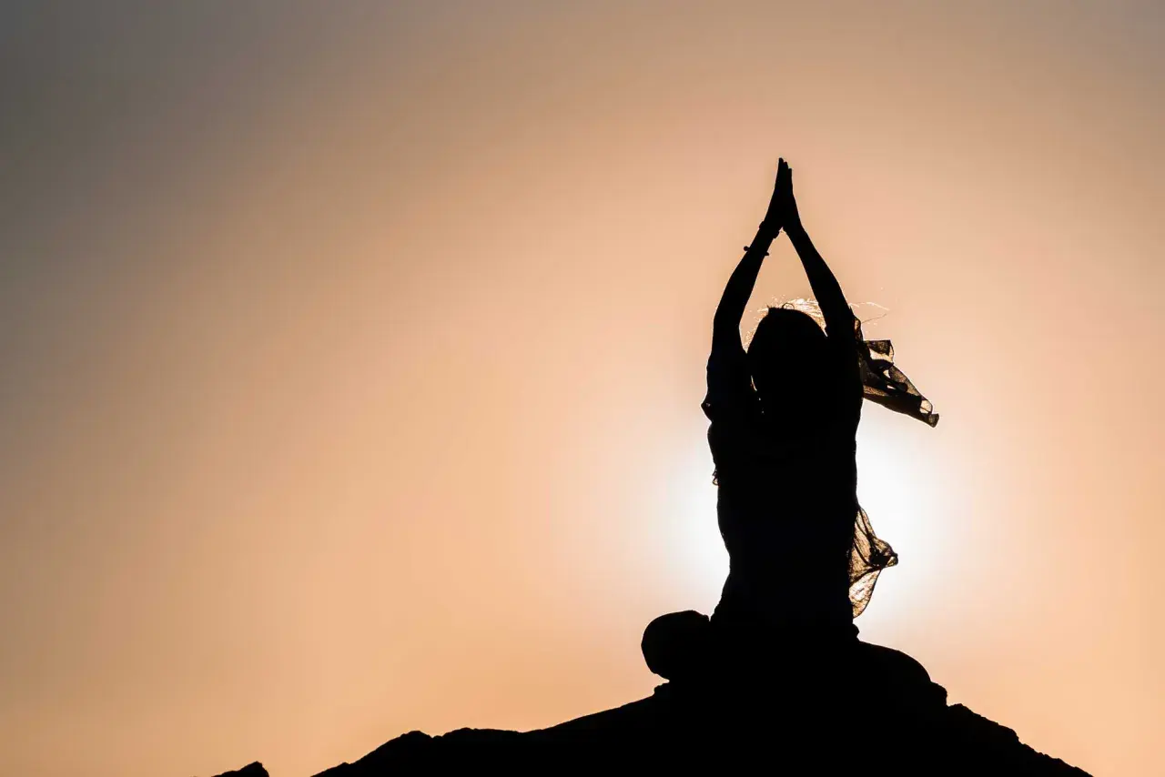 Silhouette einer Person in meditativer Haltung mit erhobenen Händen, die innere Freiheit verkörpert.