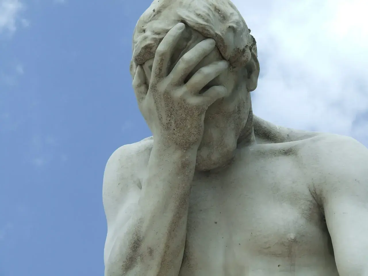 Marmorstatue mit verdecktem Gesicht im blauen Himmel. Ein Symbol für das Aushalten von Schmerzen, Tipps zur Bewältigung.