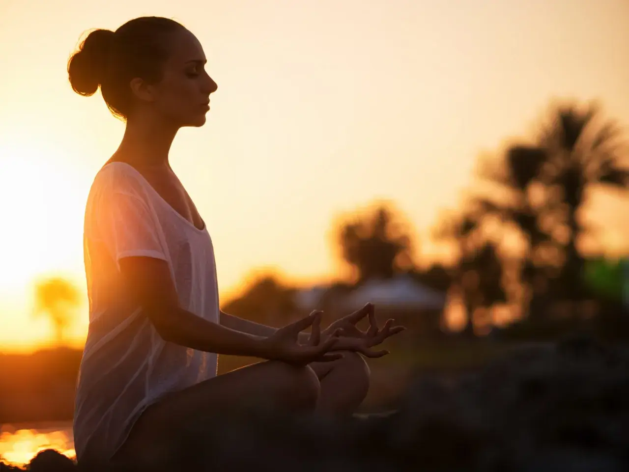 Frau in Meditation am Strand bei Sonnenuntergang, Gedanken loslassen.