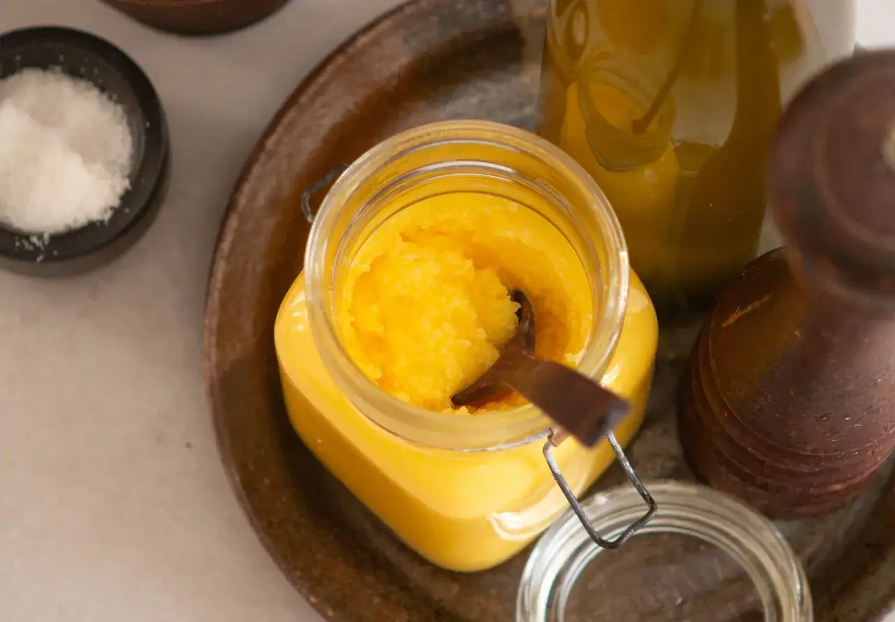 Ein Glas mit leuchtend gelbem Ghee, daneben eine Sch&uuml;ssel mit Salz und ein Pfefferm&uuml;hlen-&auml;hnliches Objekt. Ghee ist gekl&auml;rte Butter.