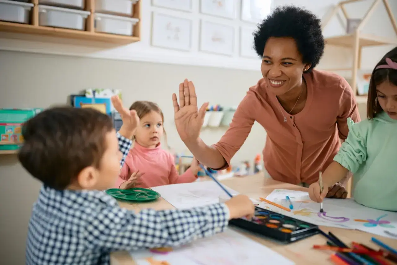 Lehrerin gibt High-Five, während Kinder malen. Trotz des Trubels strahlt sie.