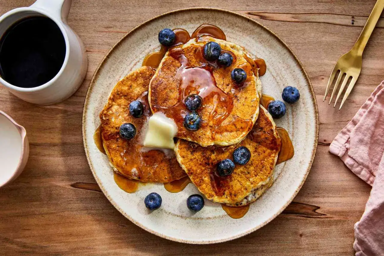Ein Stapel goldbrauner Pfannkuchen mit Blaubeeren, Butter und Sirup. Ein k&ouml;stliches Fr&uuml;hst&uuml;ck mit komplexen Kohlenhydraten, serviert mit Kaffee.