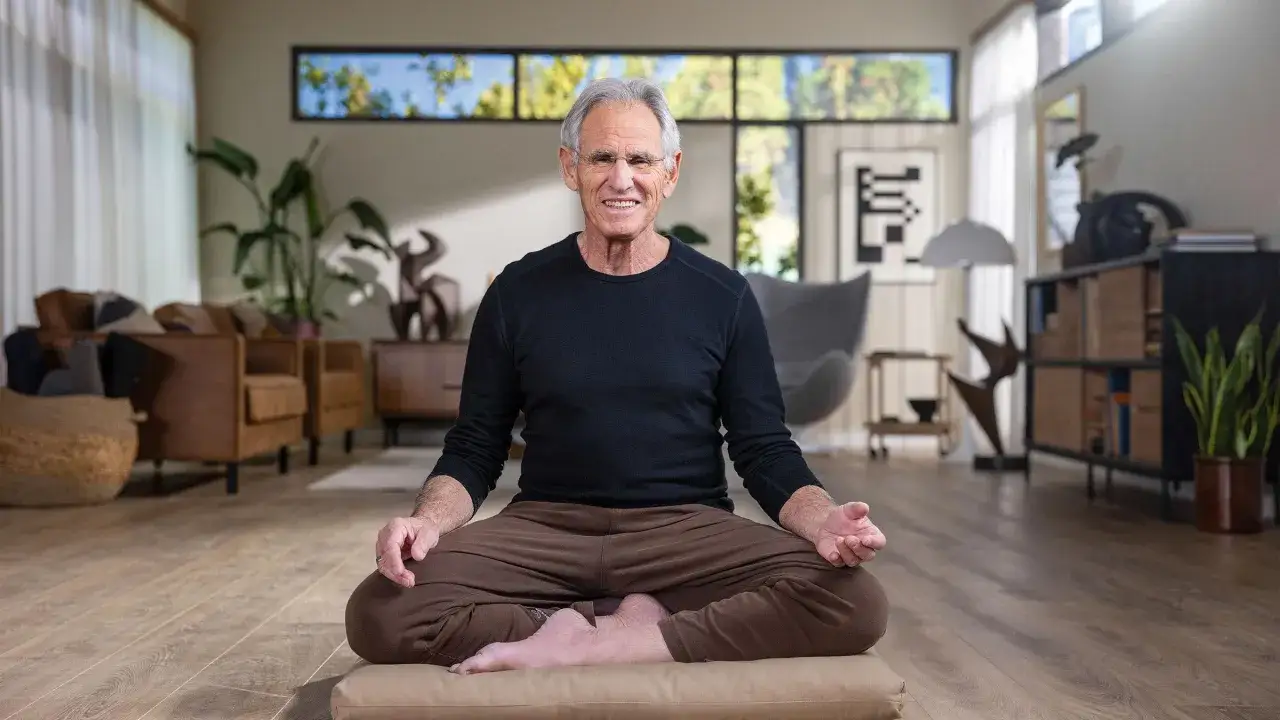 Ein Mann in Meditationshaltung, inspiriert von Jon Kabat-Zinn Zitaten, l&auml;chelt in einem modernen Wohnzimmer.