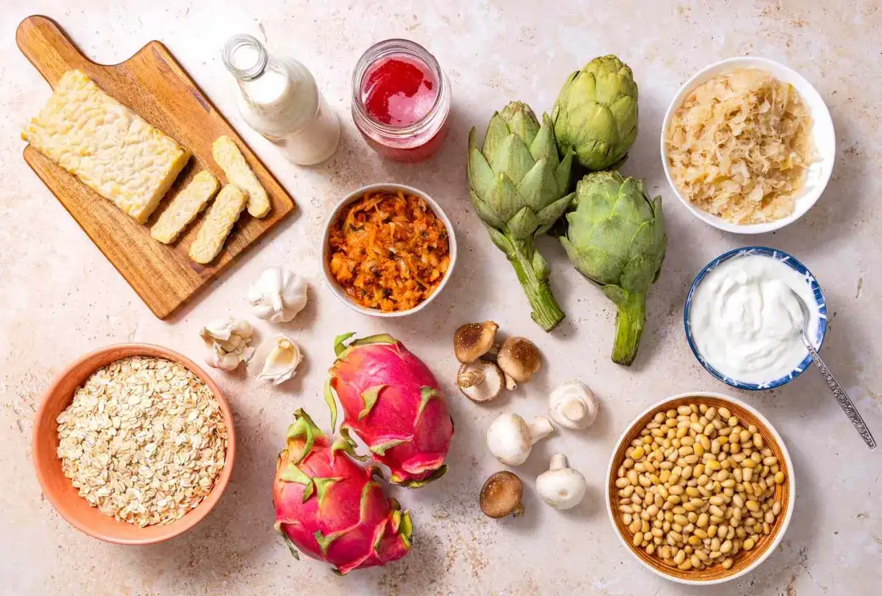 Vielfalt an verdauungsanregenden Lebensmitteln: Tempeh, Haferflocken, Sauerkraut, Joghurt, Artischocken, Pilze, Sojabohnen, Drachenfrucht und Knoblauch.