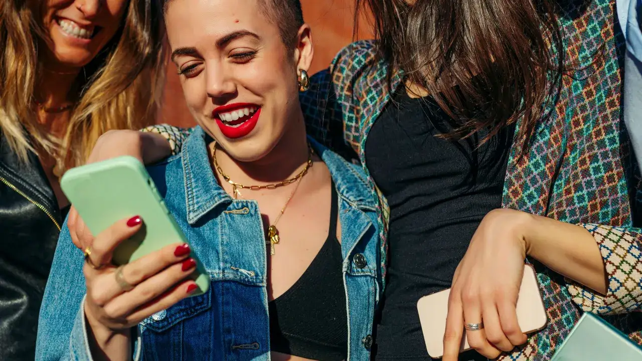 Drei Freundinnen lachen und teilen Handy-Inhalte. Selbst wenn sie sich nicht oft sehen, ist ihre Freundschaft stark.