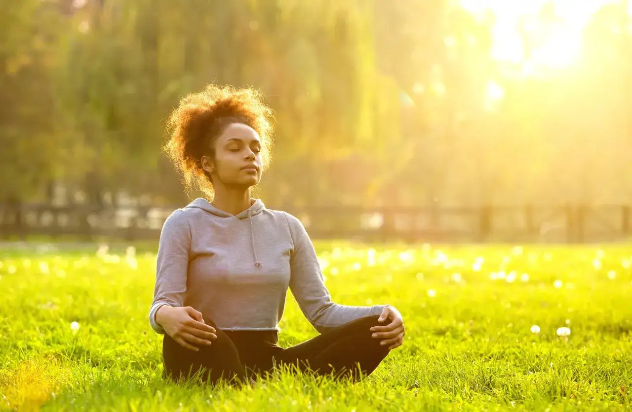 Junge Frau in der Natur bei Sonnenuntergang, die eine Atem Meditation praktiziert.