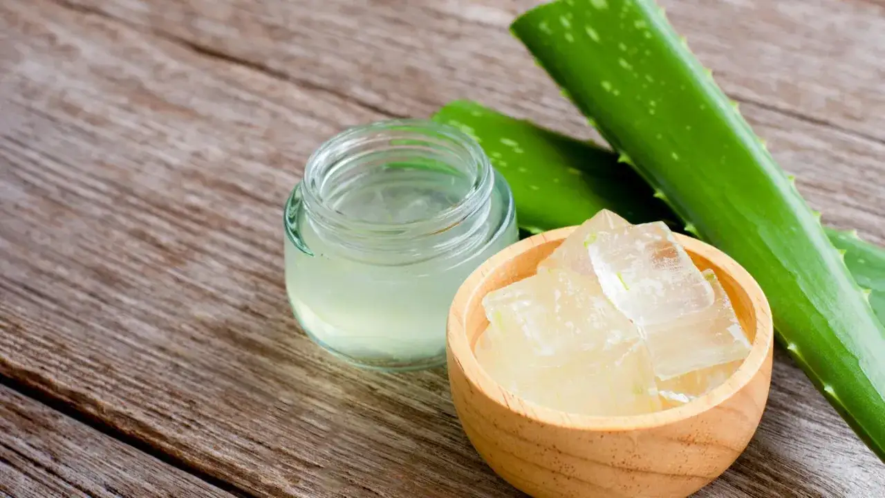 Frische Aloe Vera Blätter und gewürfeltes Gel in einer Holzschale, daneben ein Glas mit fertigem Aloe Vera Gel. So einfach lässt sich Aloe Vera Gel herstellen.
