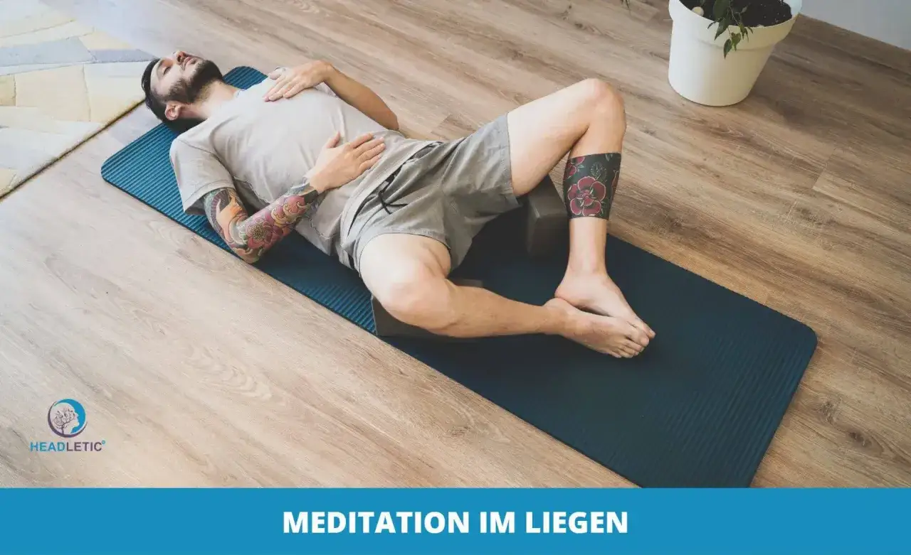 Mann mit Tattoos entspannt sich im Liegen auf einer Yogamatte, umgeben von Holzboden und einer Pflanze.