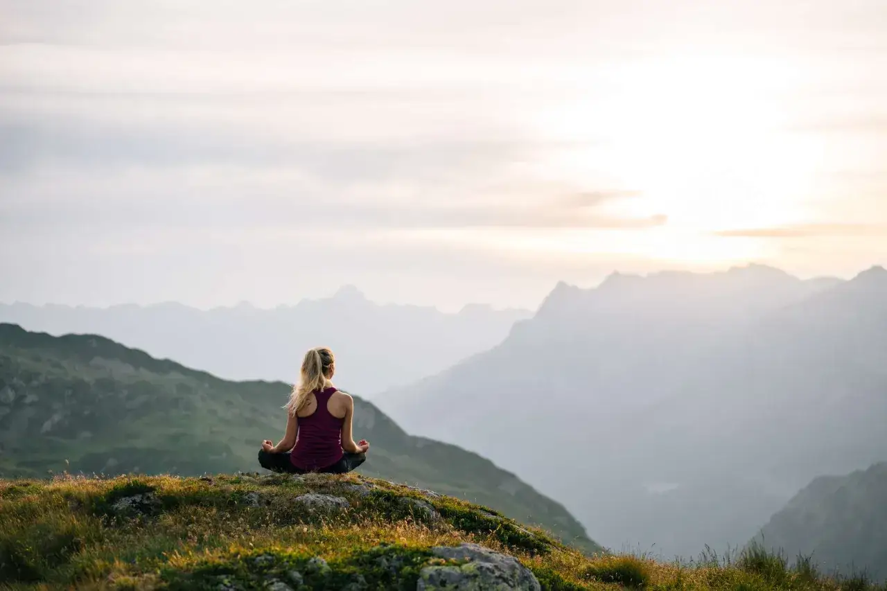 Frau meditiert auf einem Berg. Das ist ein Retreat: Stille, Natur und Selbstfindung.
