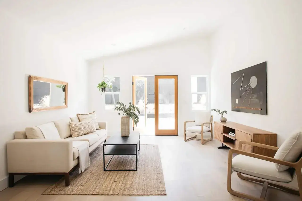 Helles Wohnzimmer mit beigem Sofa, Holzakzenten und Pflanzen. Ein Spiegel und ein Kunstwerk unterstreichen den achtsamen Minimalismus.
