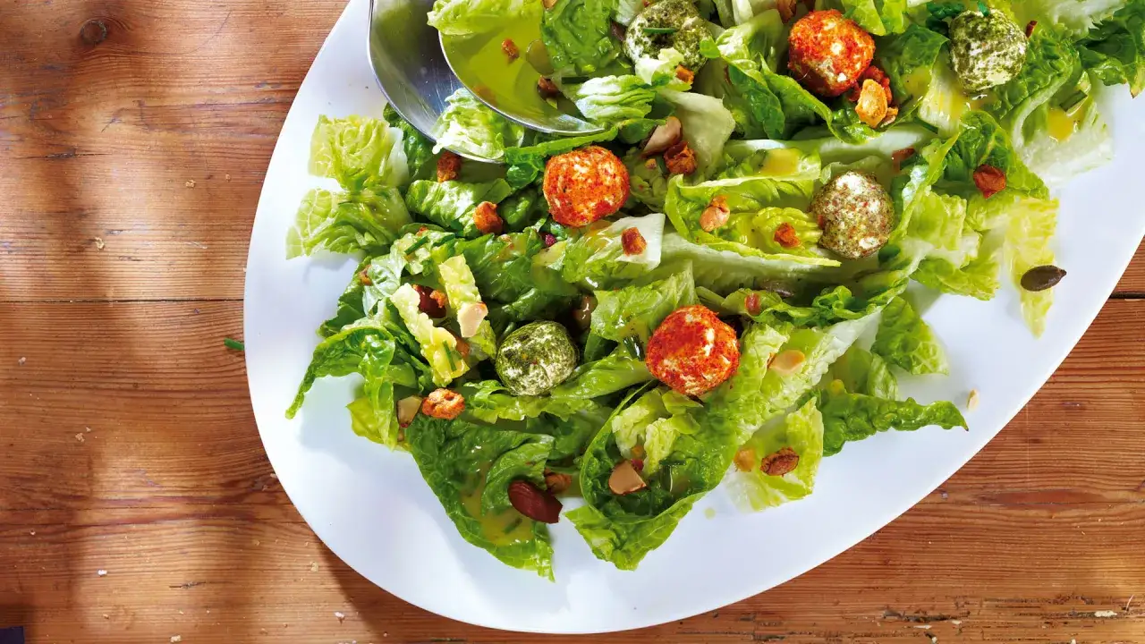 Frischer Romana Salat mit bunten K&auml;seb&auml;llchen, N&uuml;ssen und Kernen, appetitlich auf einem wei&szlig;en Teller angerichtet.