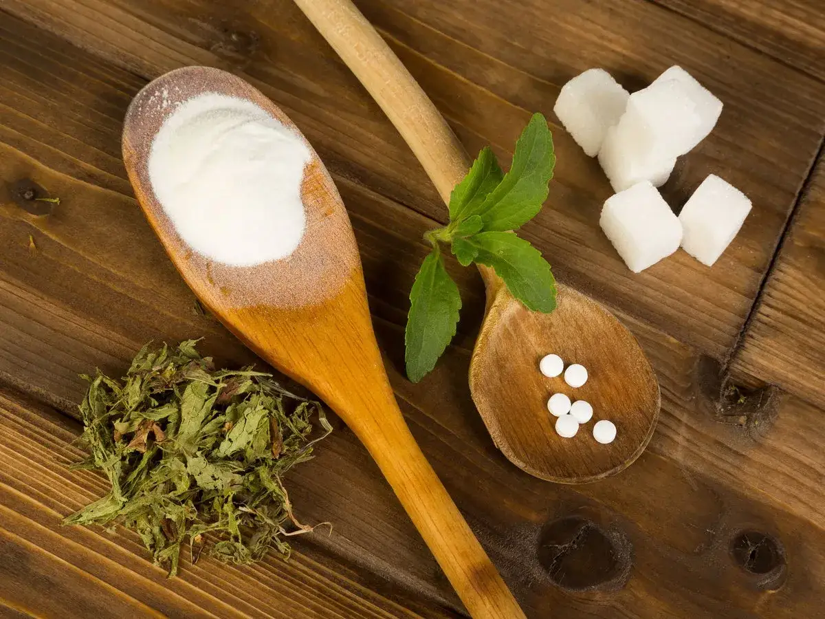 Holzkochl&ouml;ffel mit Stevia-Pulver, getrockneten Stevia-Bl&auml;ttern, Stevia-Tabletten und Zuckerw&uuml;rfeln. M&ouml;gliche Stevia Nachteile werden hier visuell angedeutet.