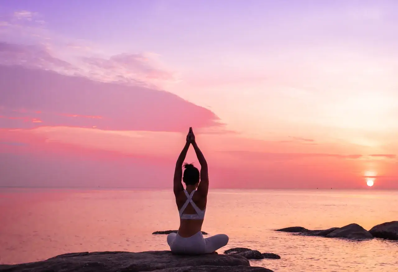Frau in Yoga-Pose am Meer bei Sonnenaufgang. Sie spürt, was Yoga mit der Seele macht: Ruhe und Einklang.
