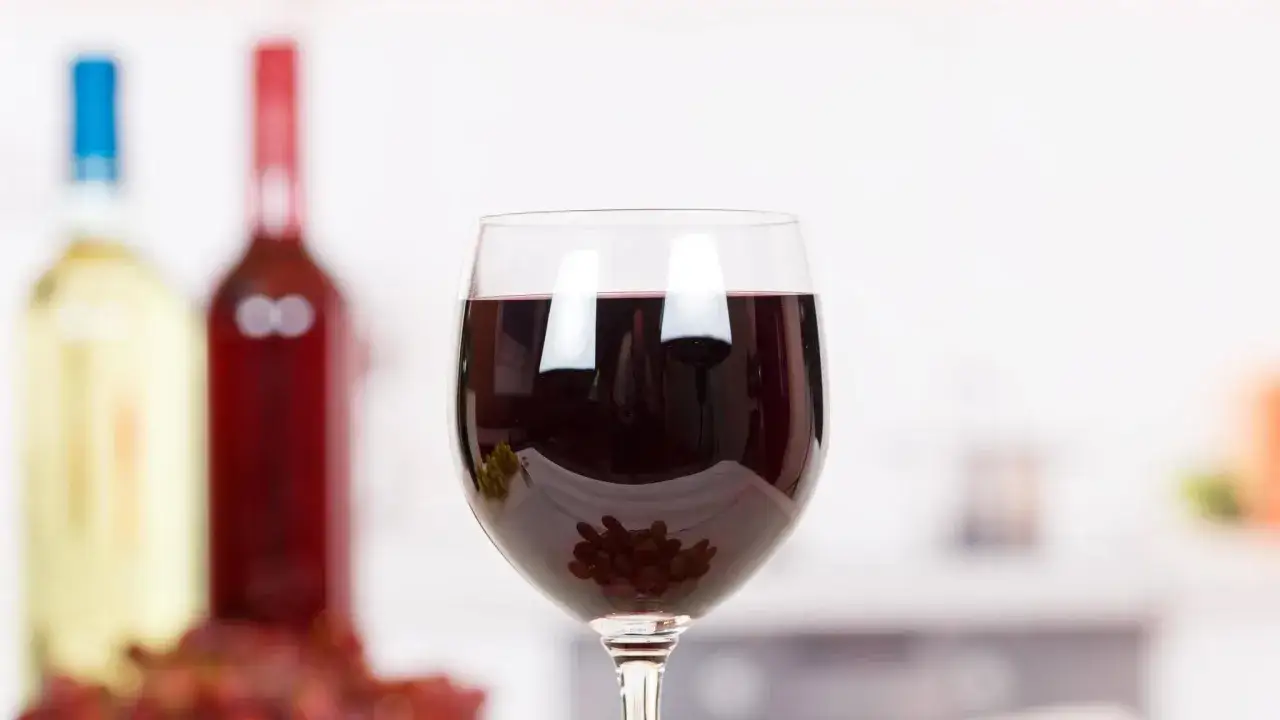 Ein Glas Rotwein am Abend, mit Trauben und Flaschen im Hintergrund.