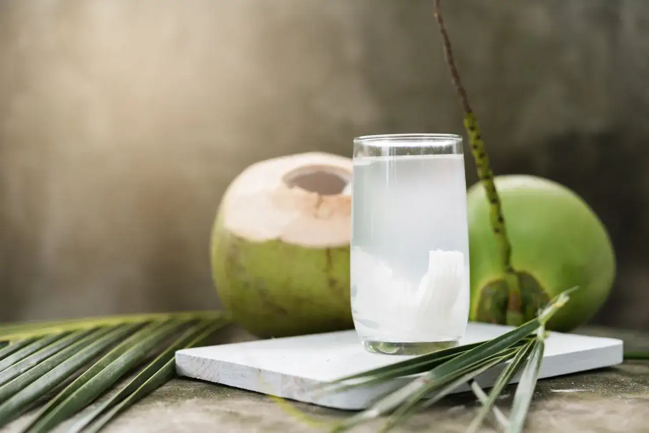 Erfrischendes Kokoswasser im Glas, daneben eine ge&ouml;ffnete Kokosnuss. Perfekt f&uuml;r leichte Kokoswasser Rezepte.