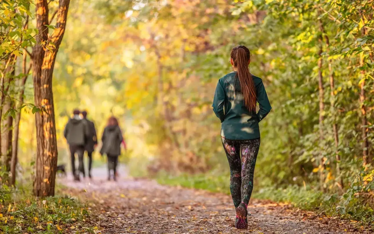 Frau genießt mediatives Gehen im Herbstwald. Im Hintergrund spazieren weitere Personen.