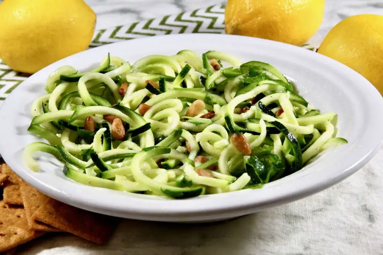 Erfrischender Zoodles Salat mit Pinienkernen und frischen Zitronen im Hintergrund. Ein leichtes und gesundes Gericht.
