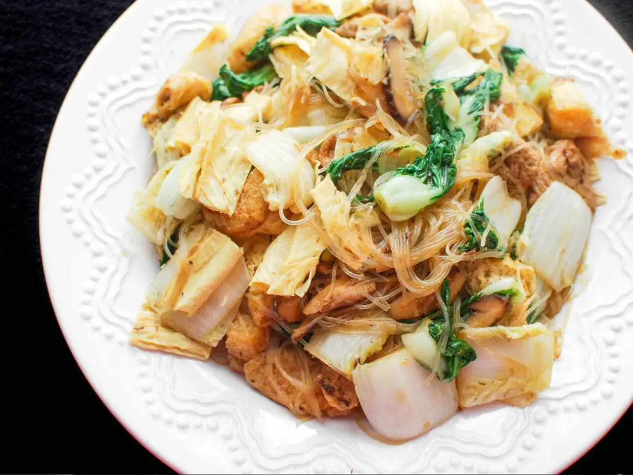 Ein Gericht, das zeigt, was Buddhisten essen: Glasnudeln mit Tofu, Pak Choi und Pilzen auf einem Teller.
