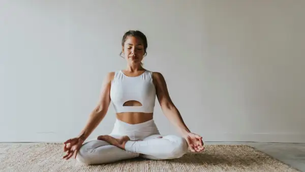 Frau in weißer Sportkleidung praktiziert Meditation. Ihre Augen sind geschlossen, Hände in Mudra-Position. Ein Bild, das Ruhe und Konzentration ausstrahlt, wie in vielen Meditation Studien.