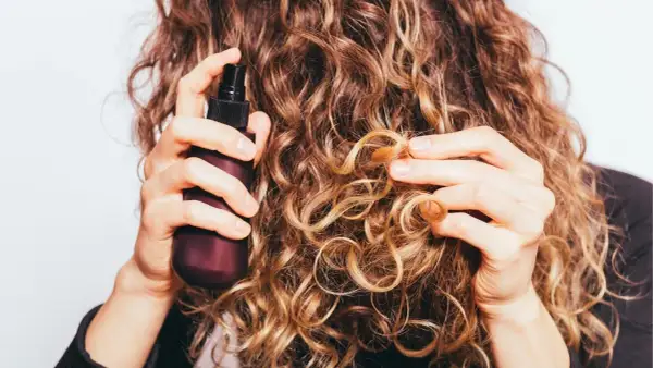 Frau sprüht mit einer Flasche auf ihre lockigen Haare. Perfekt für alle, die ihren eigenen Haarfestiger selber machen wollen.